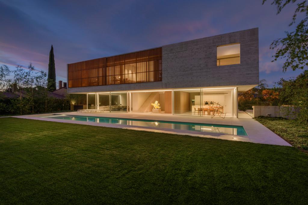Night view of Berned House in Madrid, Spain, designed by Arquitectura Estudio Berned, showcasing a solid concrete upper volume and floor-to-ceiling panoramah! ah!38 minimalist glass doors opening to the garden and pool.