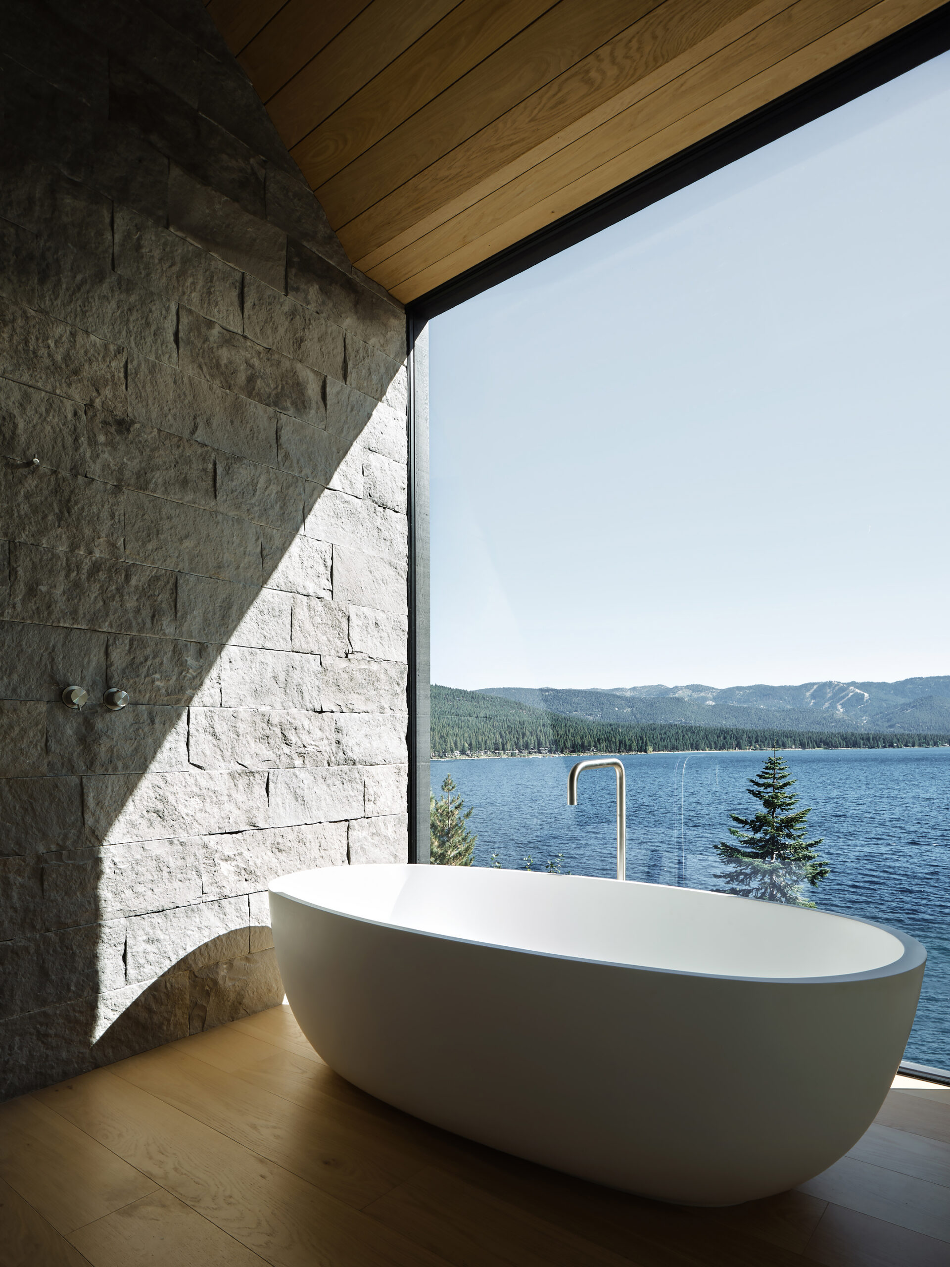 Luxurious modern bathroom with a freestanding bathtub and floor-to-ceiling panoramah! minimalist glass windows offering stunning views of Lake Tahoe and surrounding mountains.