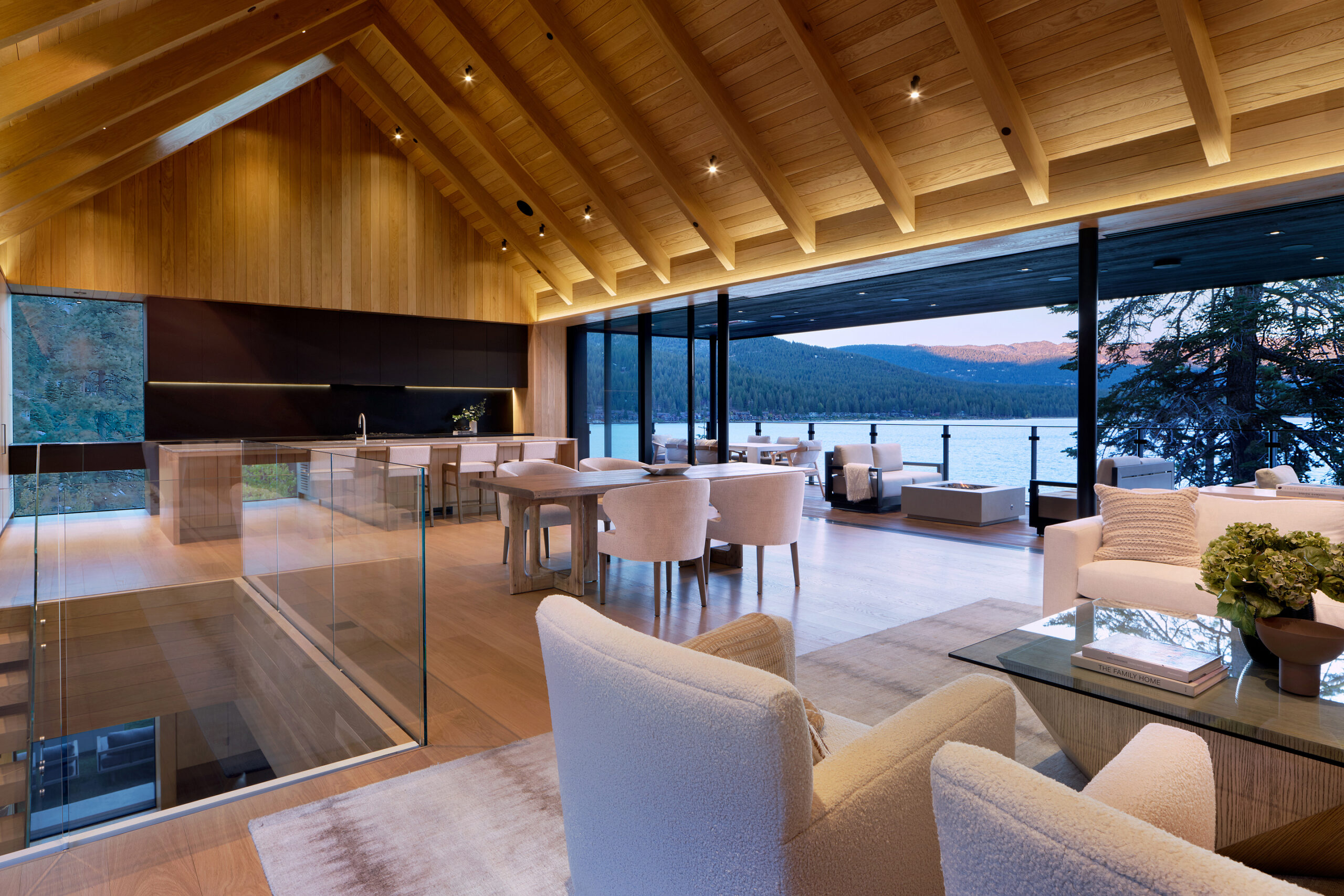 Contemporary living space with a wood-paneled ceiling, open-concept layout, and panoramah! minimalist sliding glass windows overlooking Lake Tahoe's serene waters and forested surroundings.